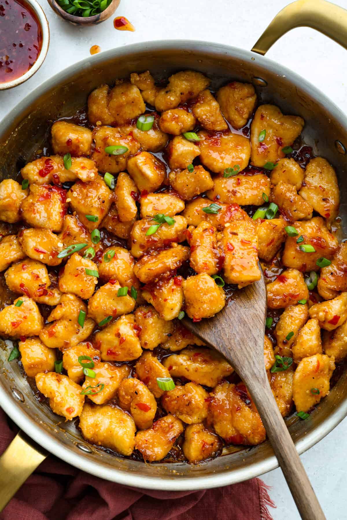 Crispy, saucy, and packed with flavor, this sweet chili chicken is a weeknight winner! Tender chicken bites get a crunchy coating, then get tossed in a sticky, sweet, and slightly spicy sauce that’s impossible to resist. Pan of sweet chili chicken garnished with green onions.