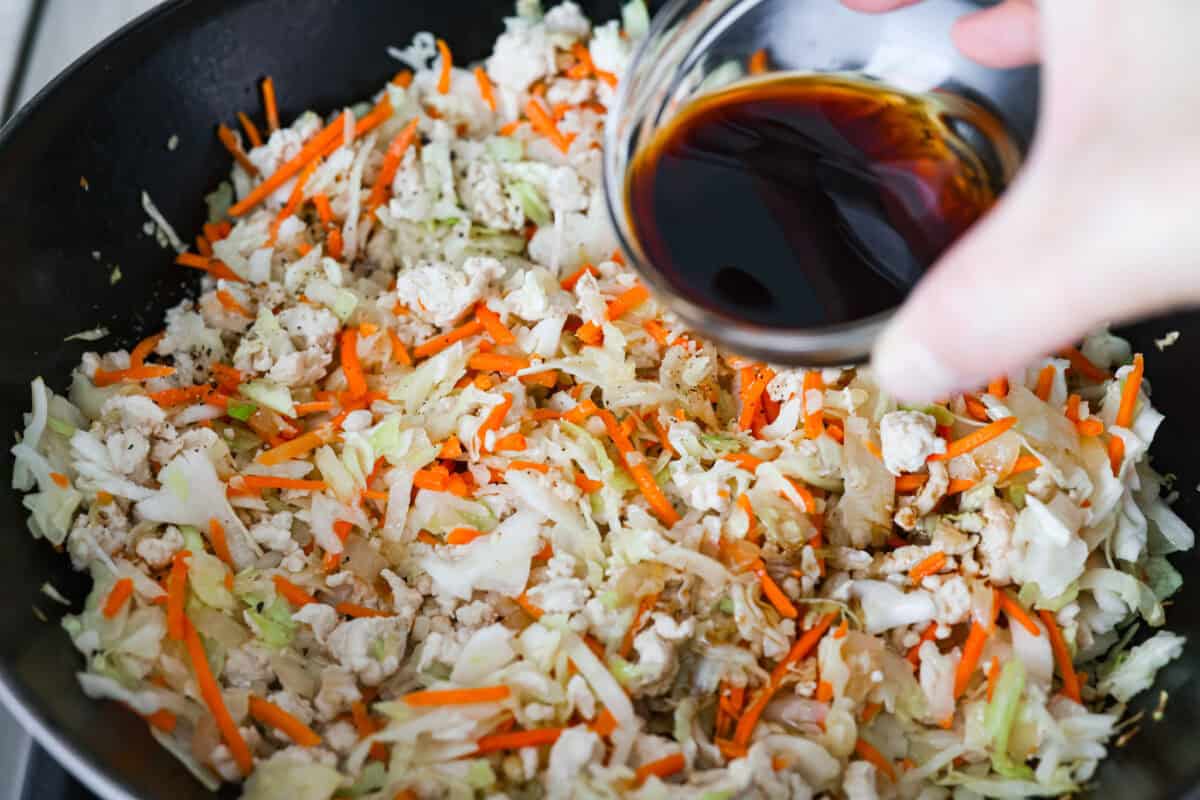 If you haven’t tried egg roll in a bowl yet, you’re in for a treat. Everything you love inside of an egg roll in a lighter, healthier, no-wrapper version! It's ready in 15 minutes, making it a perfect weeknight meal! Soy sauce being poured over the coleslaw and turkey mixture.