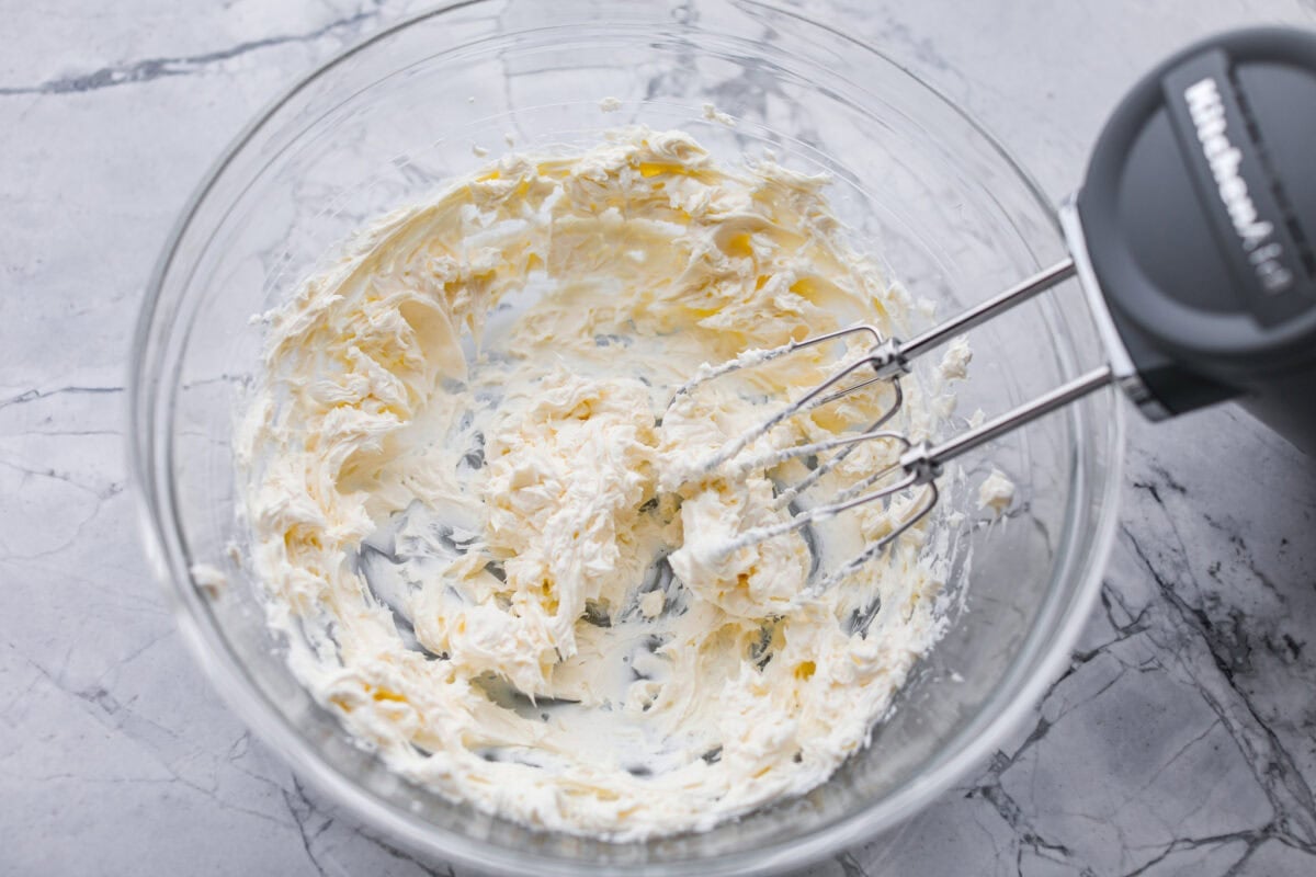 This green chile dip is warm, creamy, and so easy! The best part is, you get to control the heat! I'm telling you, the flavor hits bigger than the ingredient list! Make this for your next get-together, or let's be real, lunch! Someone using a hand mixer to beat the cream cheese in a mixing bowl.