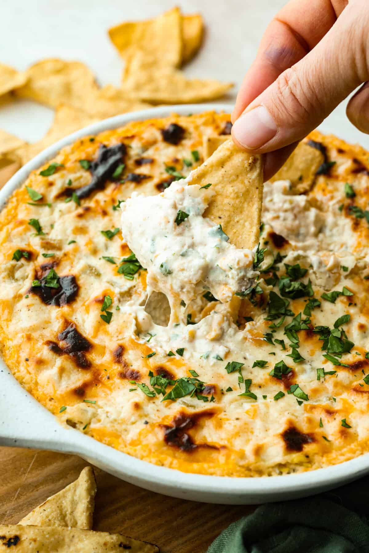 This green chile dip is warm, creamy, and so easy! The best part is, you get to control the heat! I'm telling you, the flavor hits bigger than the ingredient list! Make this for your next get-together, or let's be real, lunch! Someone scooping a bit of green chile dip onto a chip.