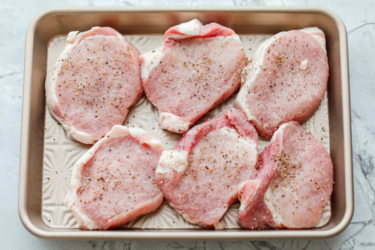 Pork chops on a cookie sheet seasoned.