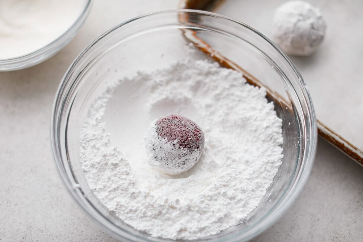 These red velvet crinkle cookies bring all the charm of classic red velvet cake in a festive, crackly cookie. With a soft center, crisp edges, and a snowy sugar coating, they’re as delicious as they are eye-catching. A cookie dough ball in a bowl of powered sugar.