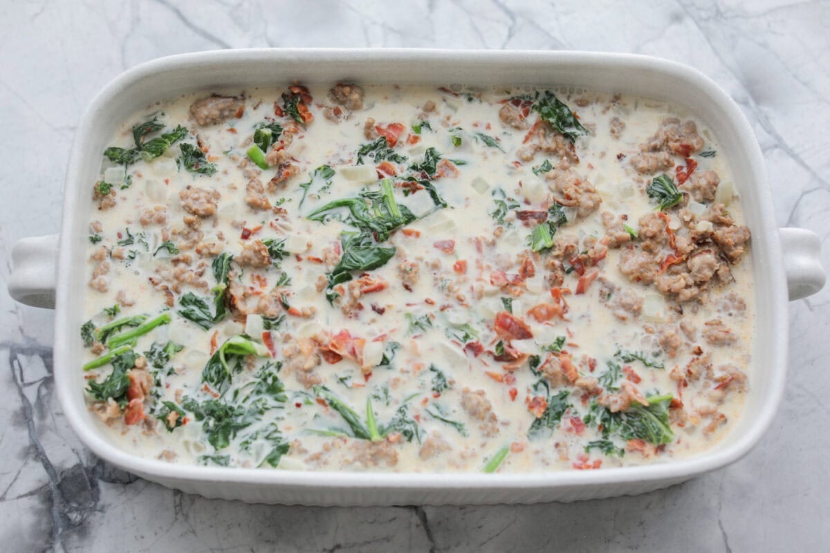 I am begging you guys to make this Zuppa Toscana Casserole! It turns the classic soup into the most delicious bake! It has layers of potatoes, sausage, bacon, kale, and cheese drenched in the most amazing sauce! Make it today, trust me! Sauce mixture poured over the potatoes in the baking dish.