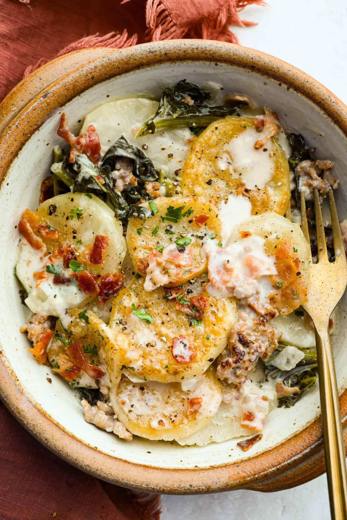 I am begging you guys to make this Zuppa Toscana Casserole! It turns the classic soup into the most delicious bake! It has layers of potatoes, sausage, bacon, kale, and cheese drenched in the most amazing sauce! Make it today, trust me! Serving size of Zuppa Toscana casserole in a bowl.
