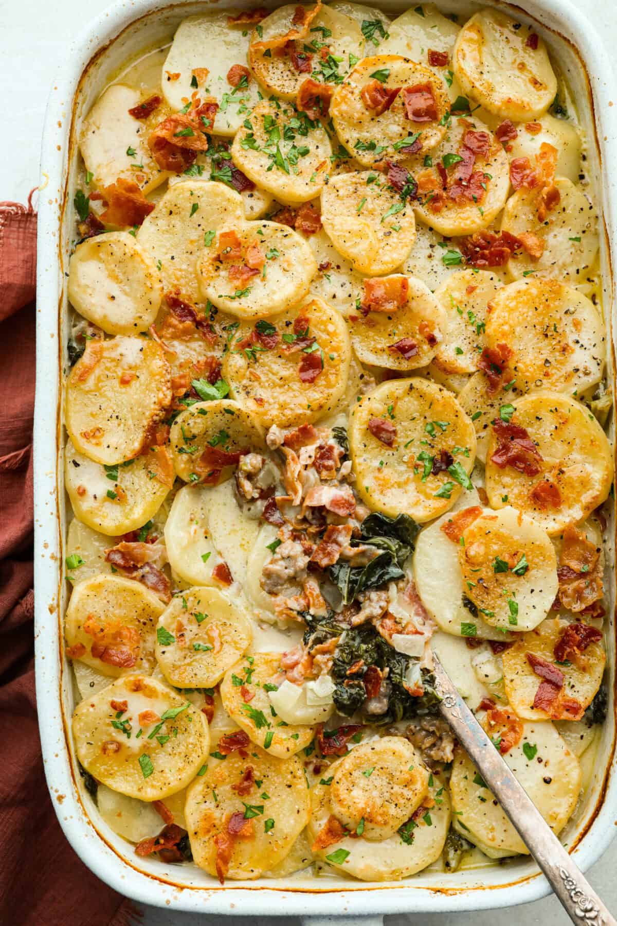I am begging you guys to make this Zuppa Toscana Casserole! It turns the classic soup into the most delicious bake! It has layers of potatoes, sausage, bacon, kale, and cheese drenched in the most amazing sauce! Make it today, trust me! Overhead shot of Zuppa Toscana casserole.
