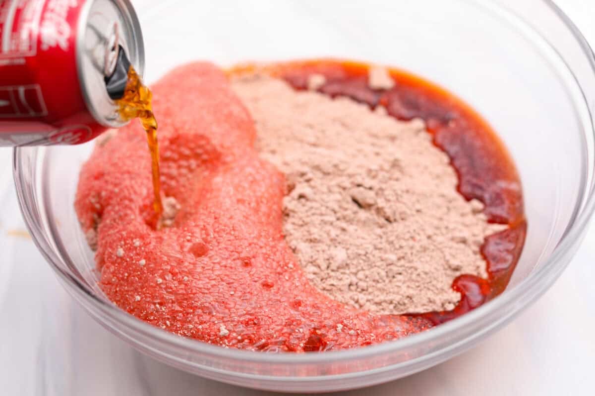 Someone pouring a can of soda into a mixing bowl with cake mix. 