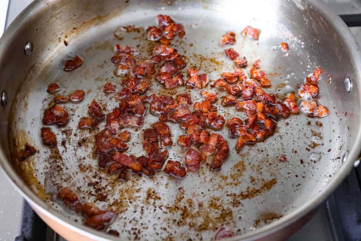Bacon pieces cooking in a skillet. 