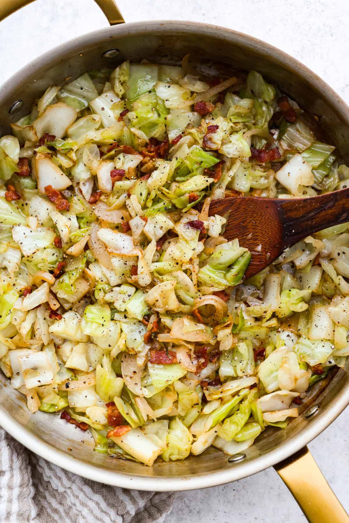 Overhead shot of fried cabbage in the skillet with a wooden spoon. 