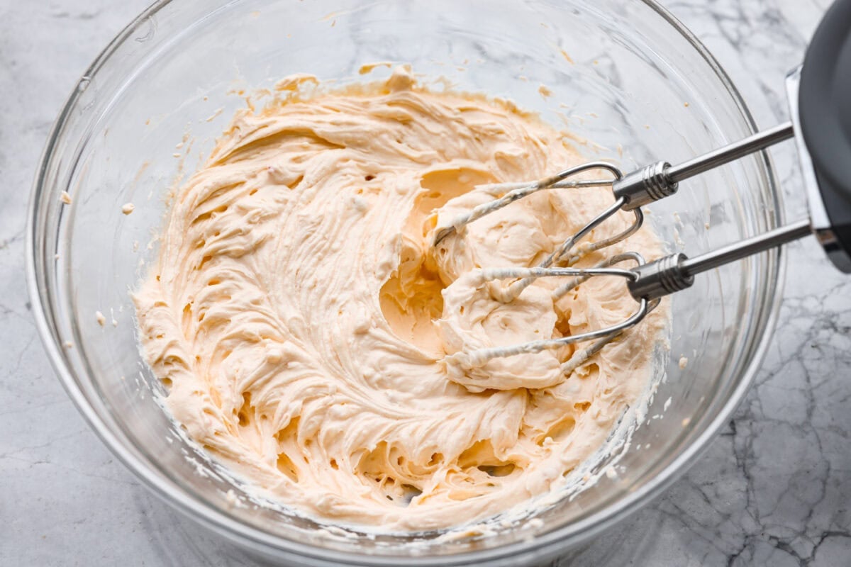 Cream cheese, sour cream and thousand island dressing being beaten with a hand mixer in a mixing bowl. 