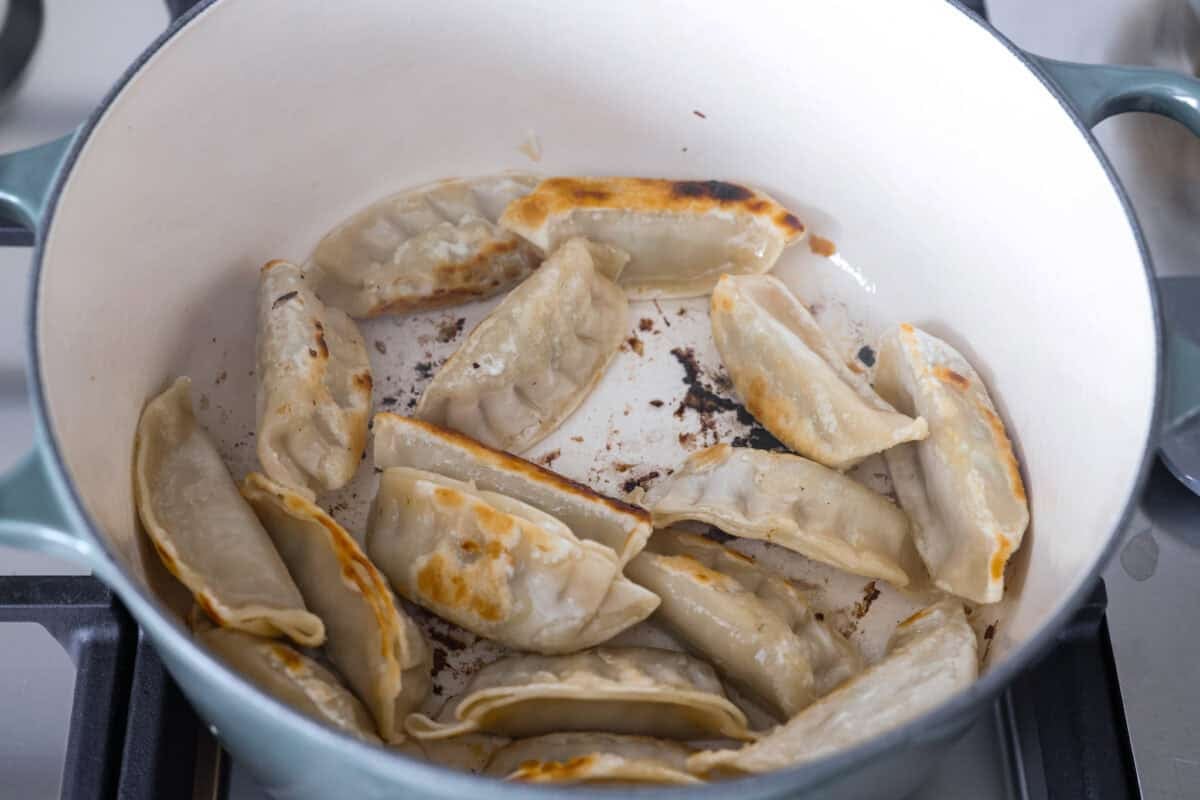 Potstickers crisping up in a pot on the stove.