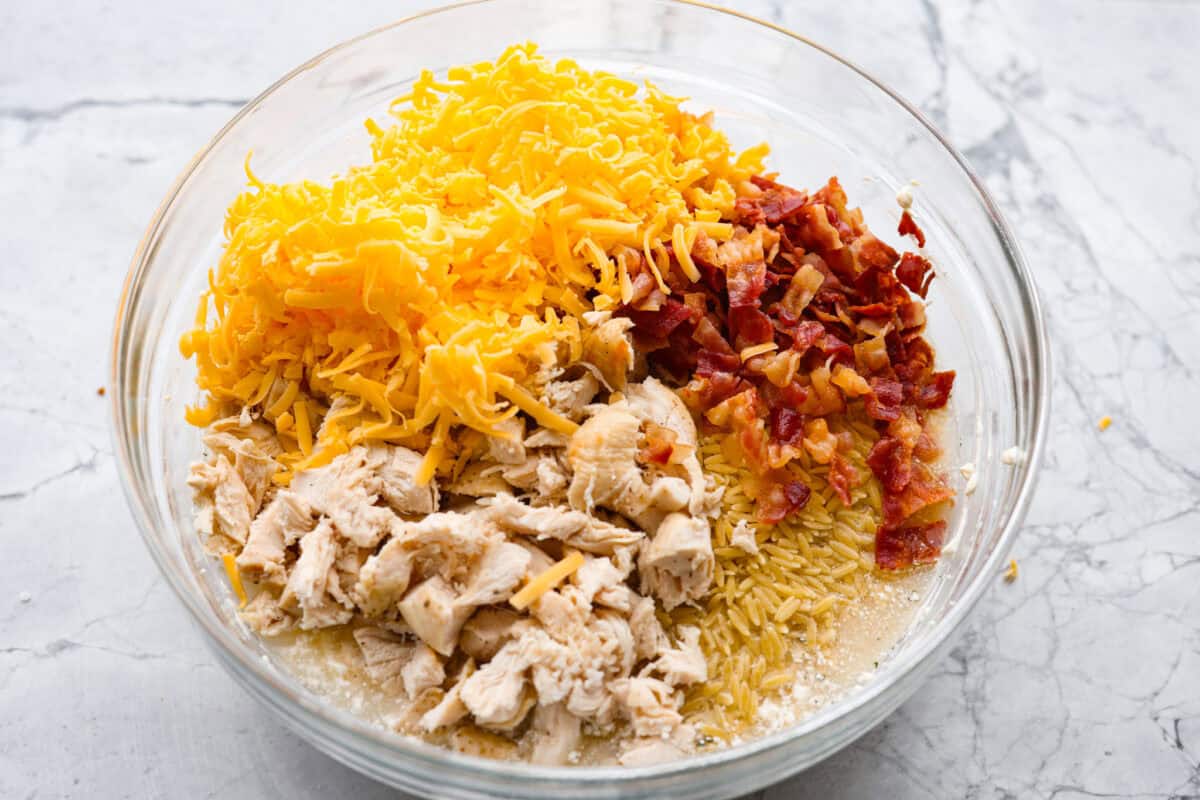 This crack orzo bake is creamy, cheesy, and packed with that irresistible ranch, bacon, and cheddar “crack” flavor everyone loves. It’s an easy casserole that’s guaranteed to be a hit. Cheese, chicken, bacon and uncooked orzo added to the bowl.