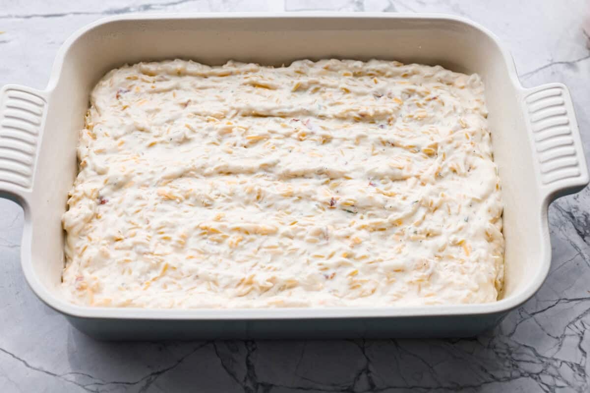 This crack orzo bake is creamy, cheesy, and packed with that irresistible ranch, bacon, and cheddar “crack” flavor everyone loves. It’s an easy casserole that’s guaranteed to be a hit. Chicken mixture spread out in a baking dish.