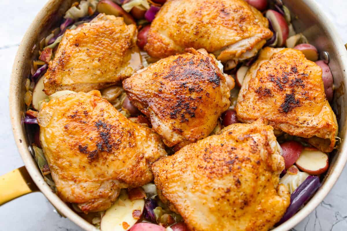 This Irish chicken is my cozy mashup of pub vibes and weeknight reality. Seared chicken thighs baked over bacon, cabbage, and potatoes, then I add a splash of Irish whiskey and a touch of cream to make the whole pan taste extra special. Chicken added to the top ready to go in the oven.