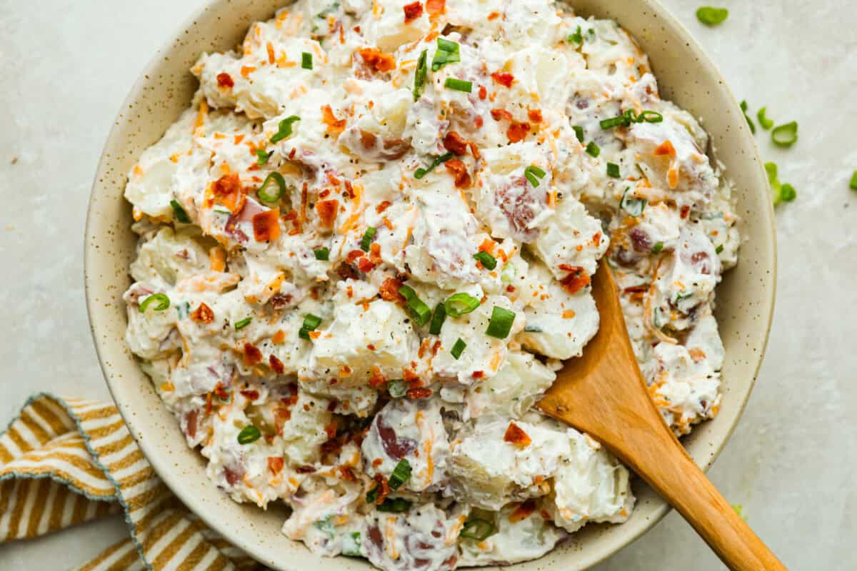 Overhead shot of crack potato salad all mixed up in a serving bowl with a wooden spoon. 