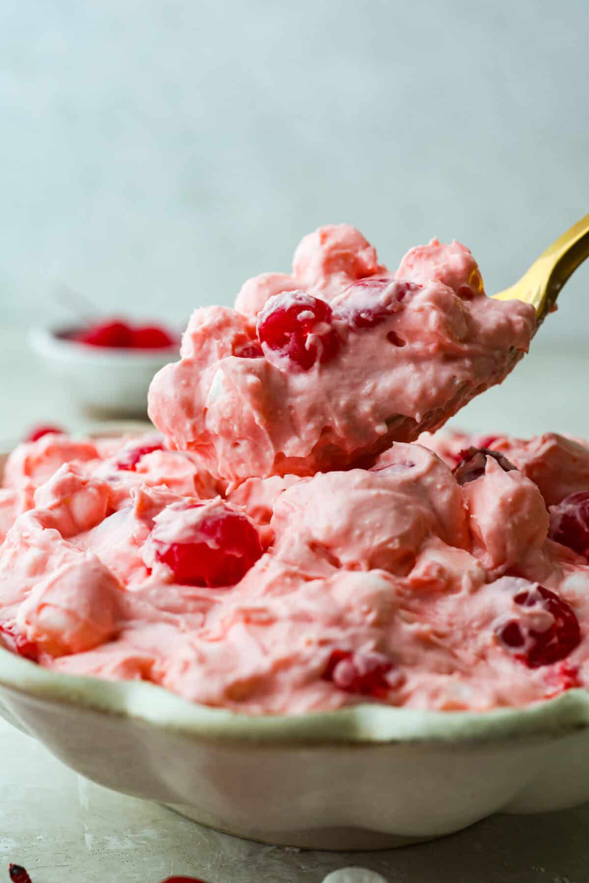Fluff salads never go out of style. They're light, creamy, and just plain fun! This cherry cheesecake fluff is customizable and so easy to throw together! It's packed with sweet-tangy cheesecake flavor and juicy cherries in every bite. Someone getting a scoop of cherry cheesecake fluff out of the bowl.
