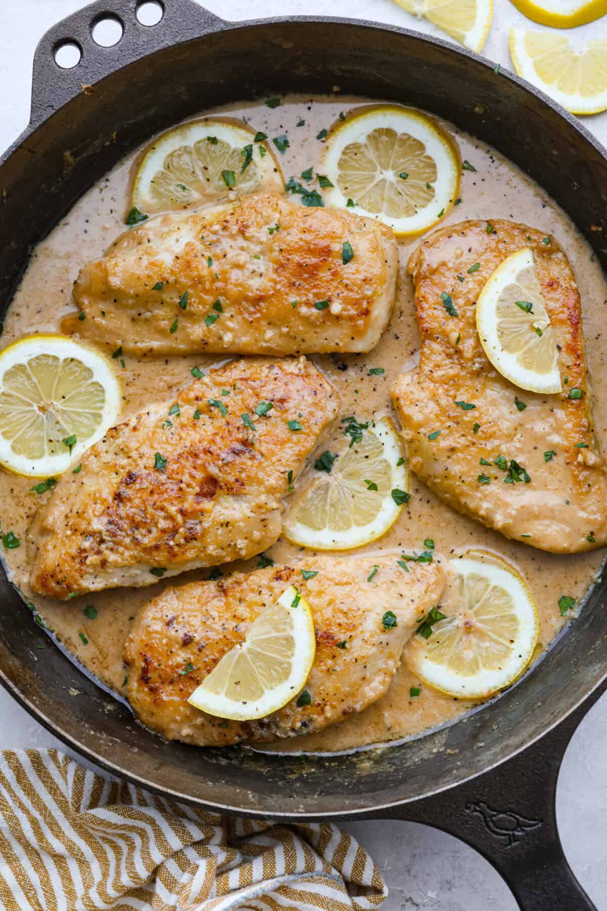 Lemon butter chicken in a skillet with slices of lemon and fresh parsley. 