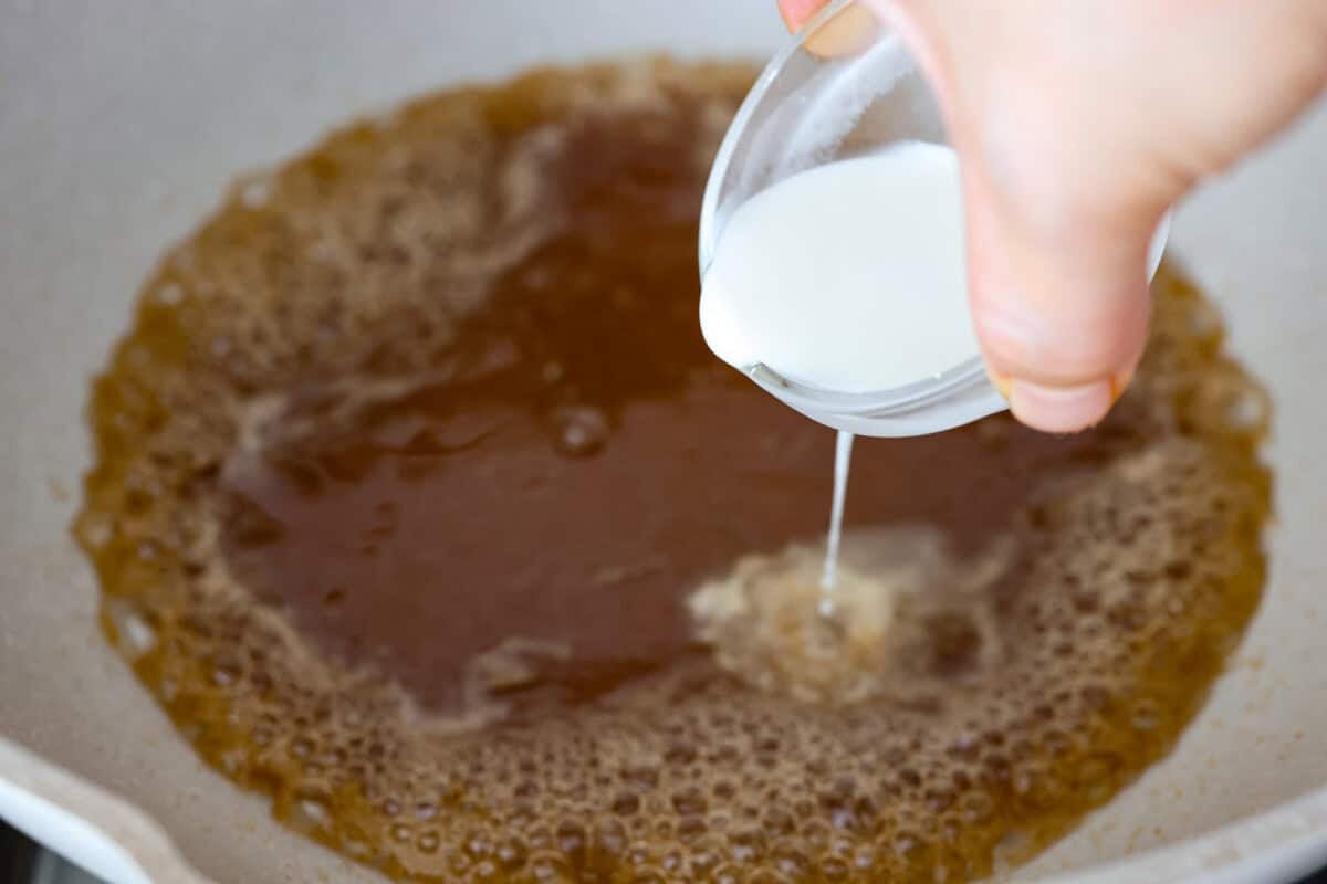 Sauce mixture cooking on the stove in a wok, with someone pouring the cornstarch slurry in to thicken. 