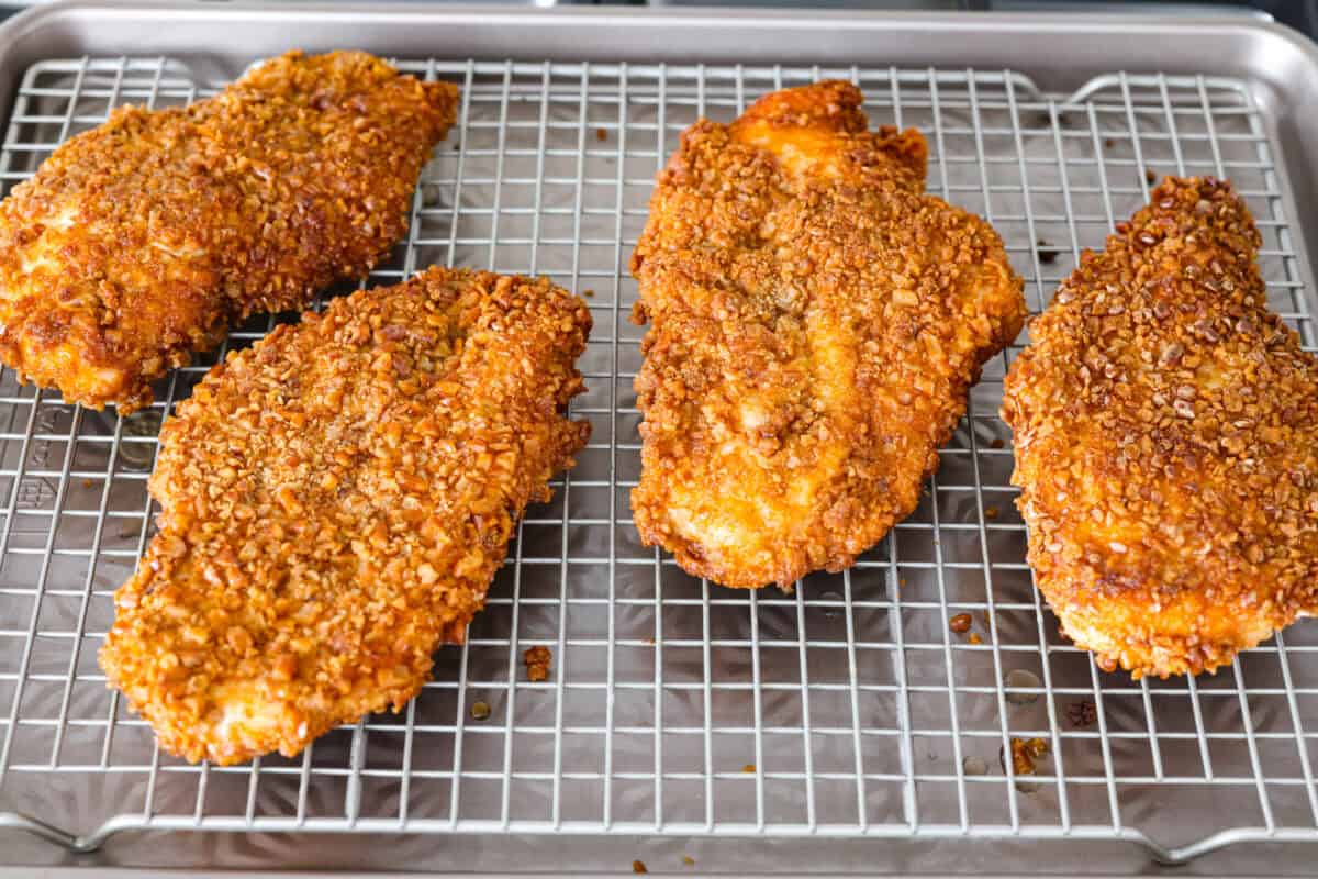 This pretzel crusted chicken takes crispy chicken to the next level. The crunchy pretzel coating adds incredible flavor and texture, making every bite extra delicious. Cooked chicken on a cooling rack.