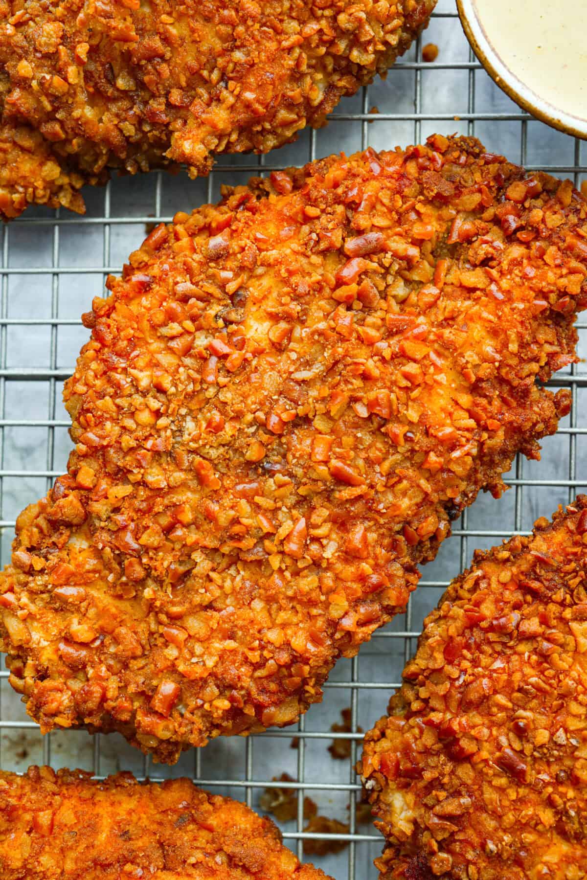 This pretzel crusted chicken takes crispy chicken to the next level. The crunchy pretzel coating adds incredible flavor and texture, making every bite extra delicious. Close up shot of the pretzel crusted chicken on the cooling rack.