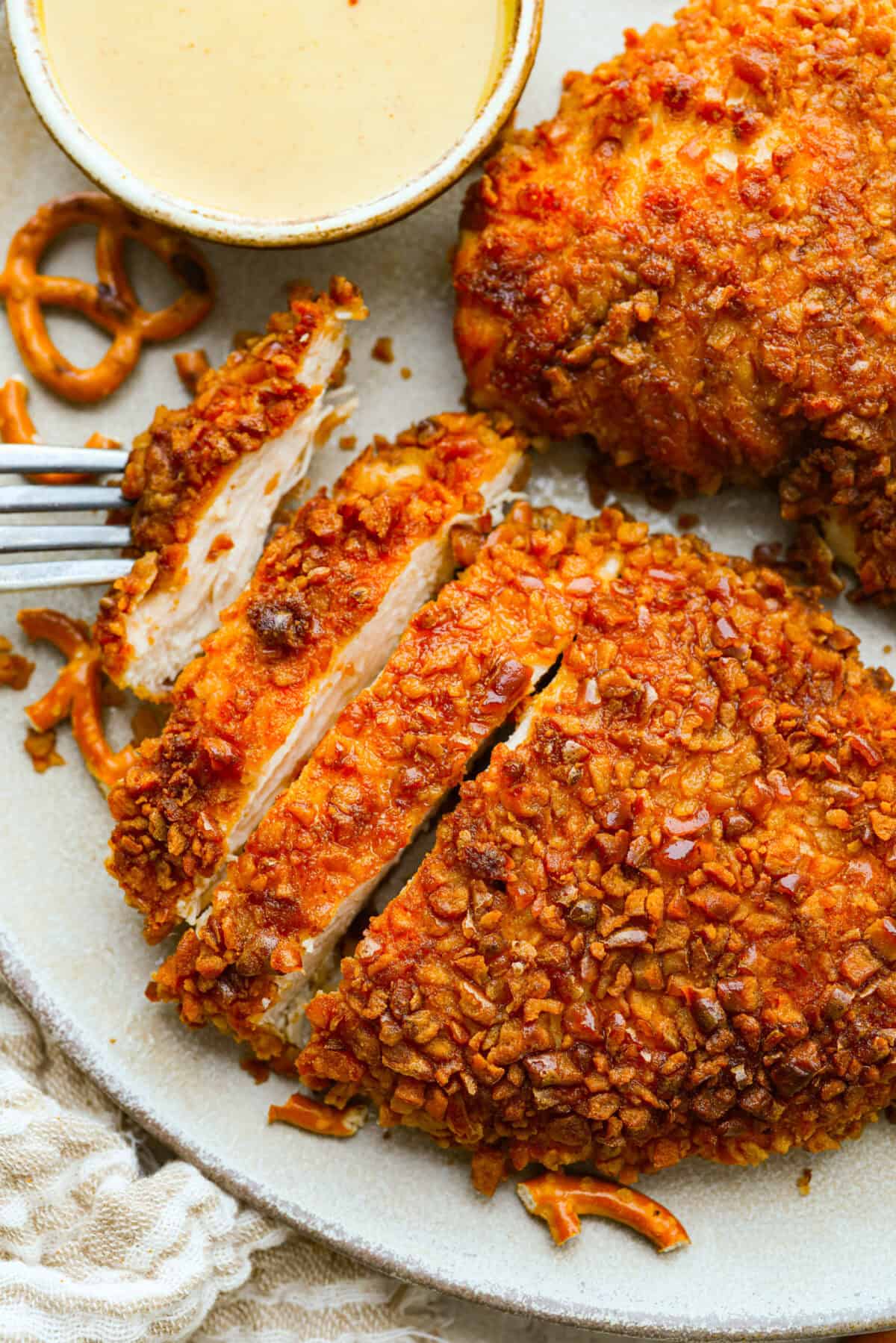 This pretzel crusted chicken takes crispy chicken to the next level. The crunchy pretzel coating adds incredible flavor and texture, making every bite extra delicious. Plated pretzel crusted chicken with a side of honey mustard sauce.
