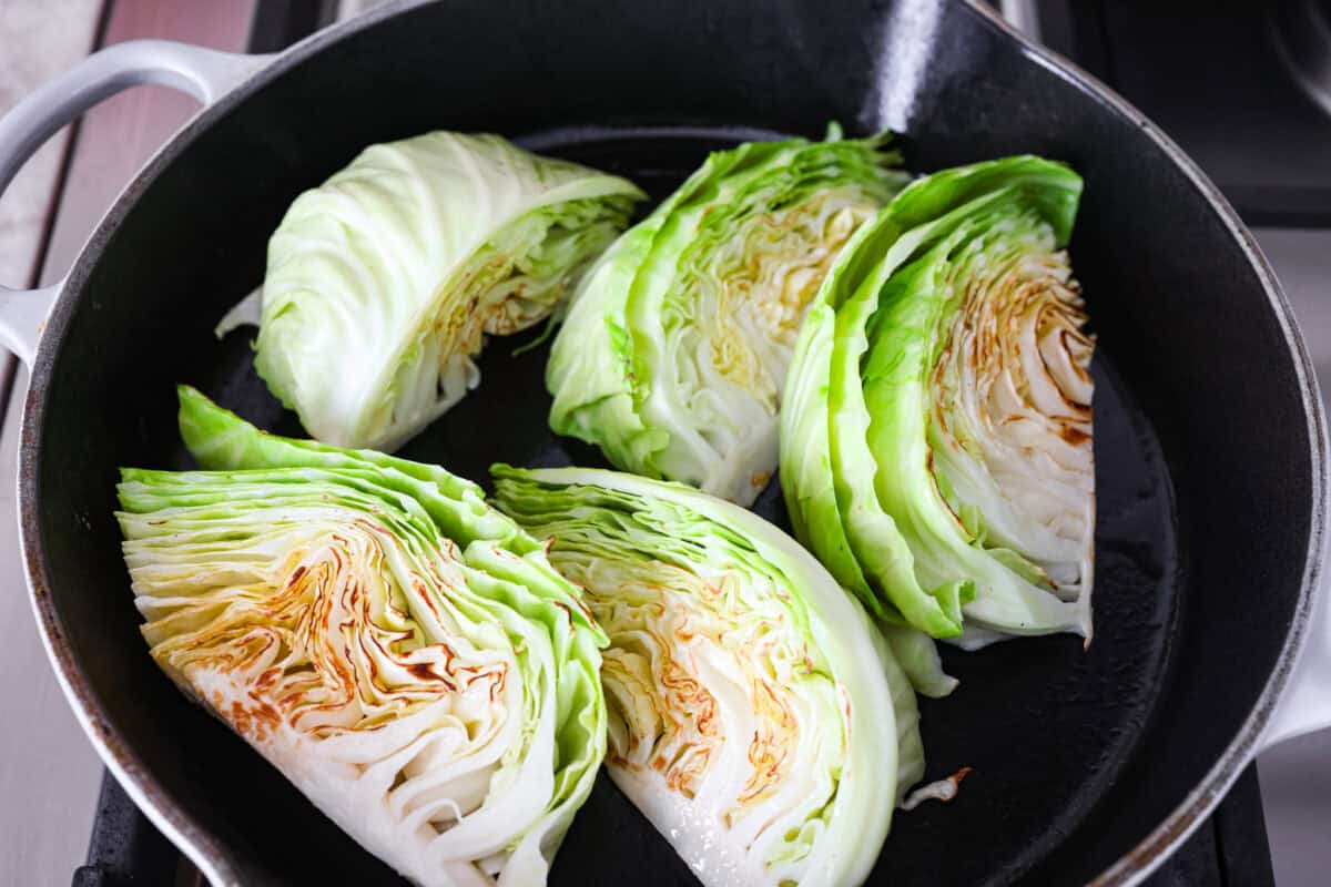 Groceries are expensive right now, so I’ve been leaning hard on the cheap staples. This melting cabbage with a garlicky cream sauce, sun-dried tomatoes, and Parmesan is easy, budget friendly, and tastes amazing. Cabbage wedges browning in a skillet.