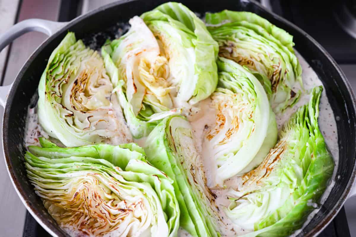 Groceries are expensive right now, so I’ve been leaning hard on the cheap staples. This melting cabbage with a garlicky cream sauce, sun-dried tomatoes, and Parmesan is easy, budget friendly, and tastes amazing. Cabbage wedges added back to the skillet.