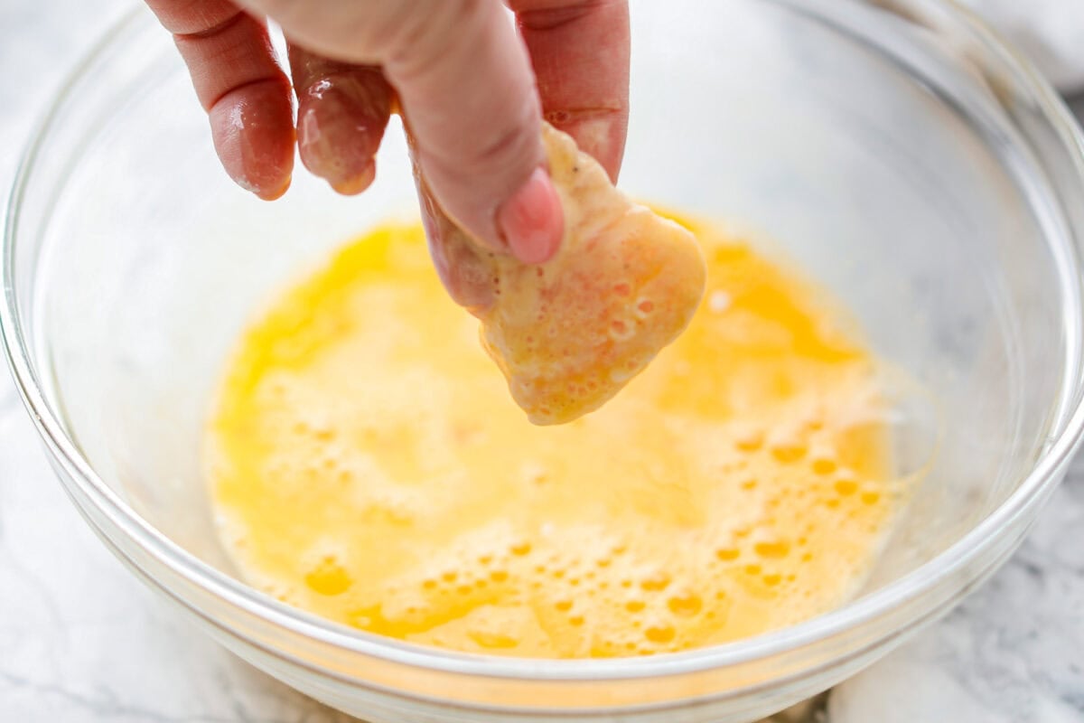 Someone coating the chicken pieces in egg. 