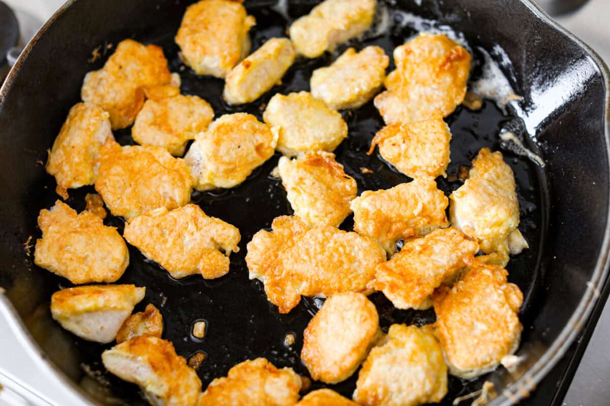 Coated chicken browning in a skillet.