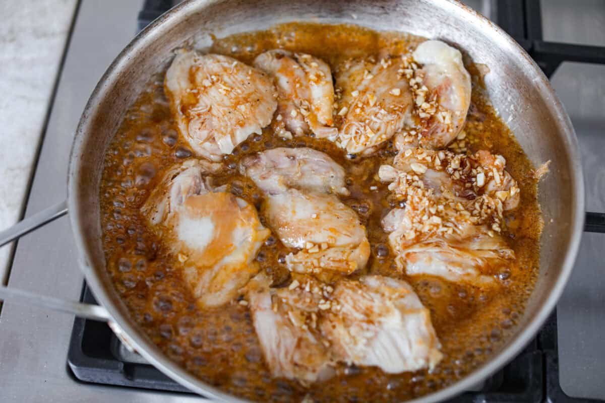 Chicken thighs cooking in a pan in the sauce. 