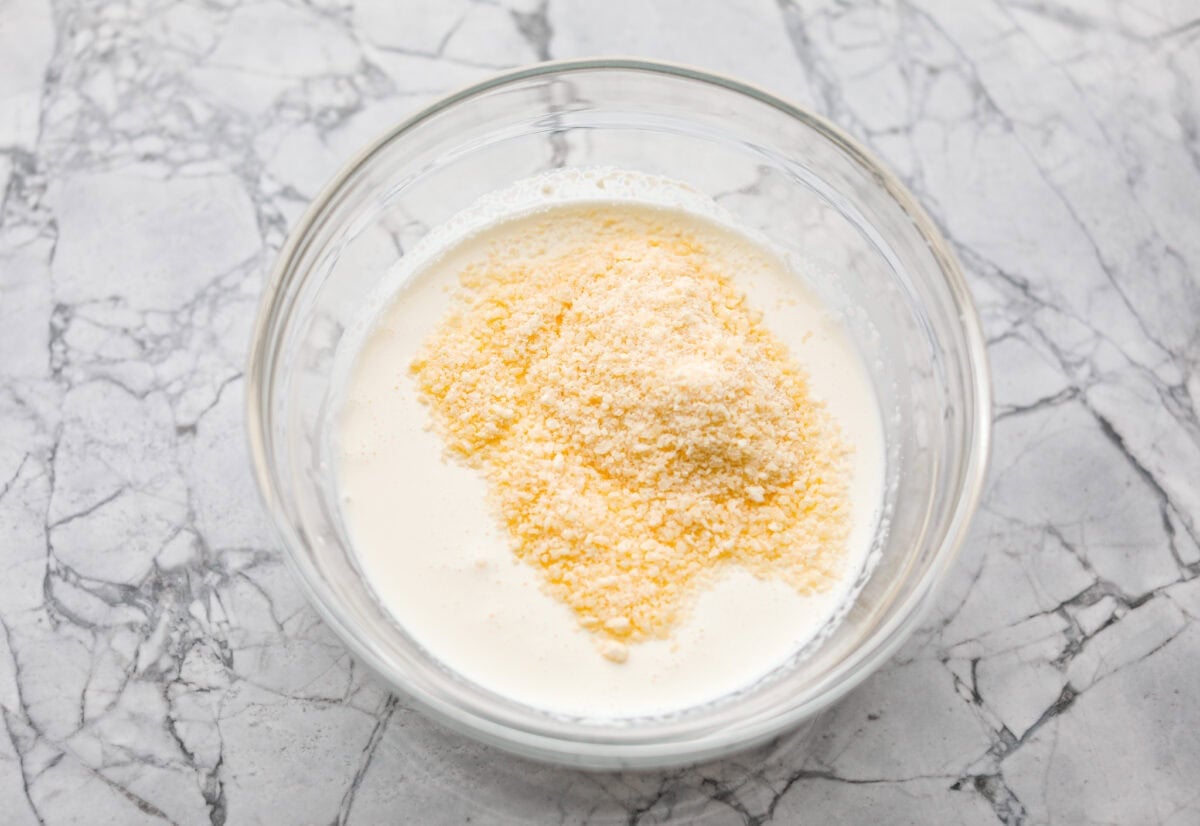 Cream cheese, cream, and parmesan cheese added to a mixing bowl. 