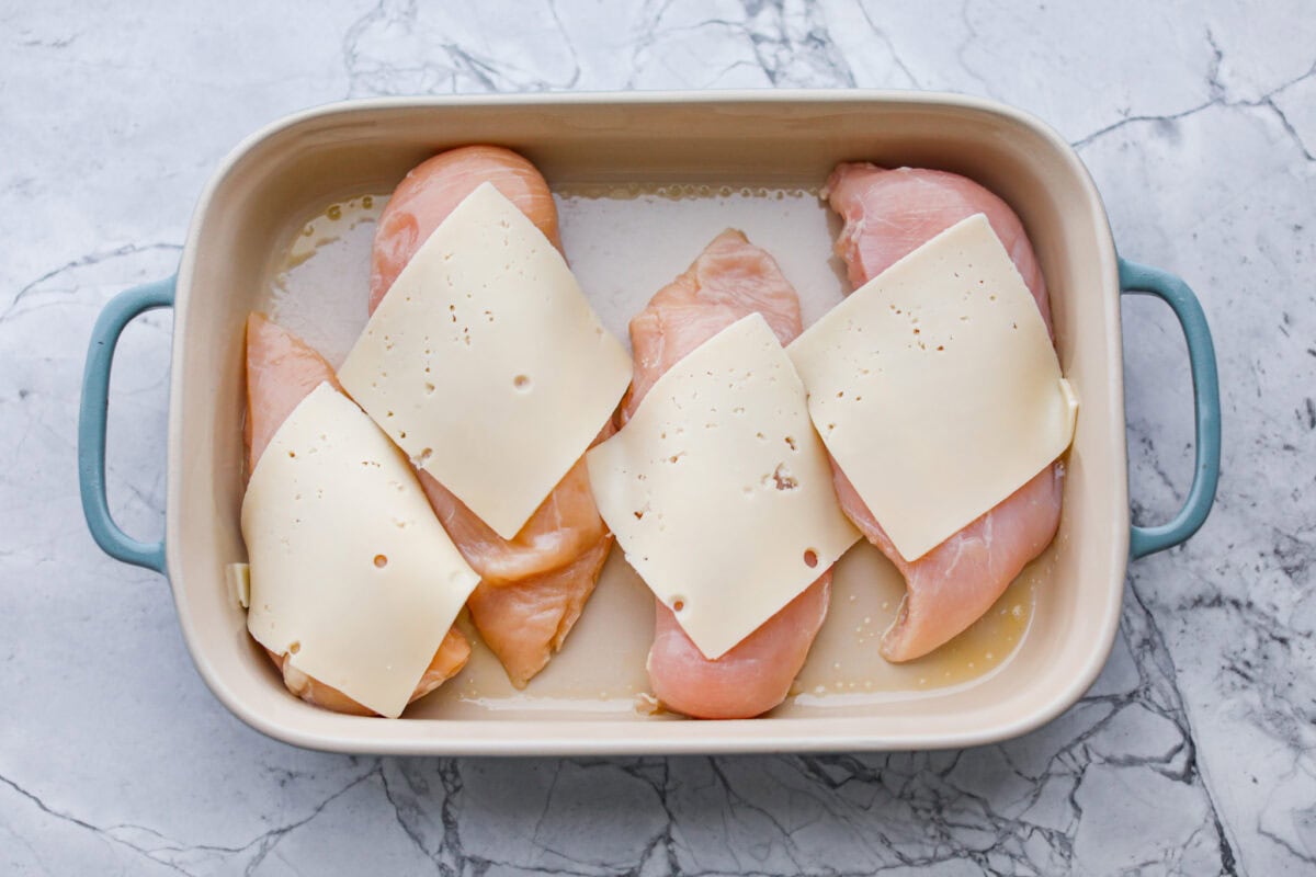 Okay, this Swiss Chicken Casserole is my go-to when I don’t feel like cooking. You basically throw it together, pop it in the oven, and somehow end up with super tender chicken, melty Swiss cheese, and the creamiest sauce. Chicken breasts in the bottom of a baking dish with a slice of Swiss cheese on top.